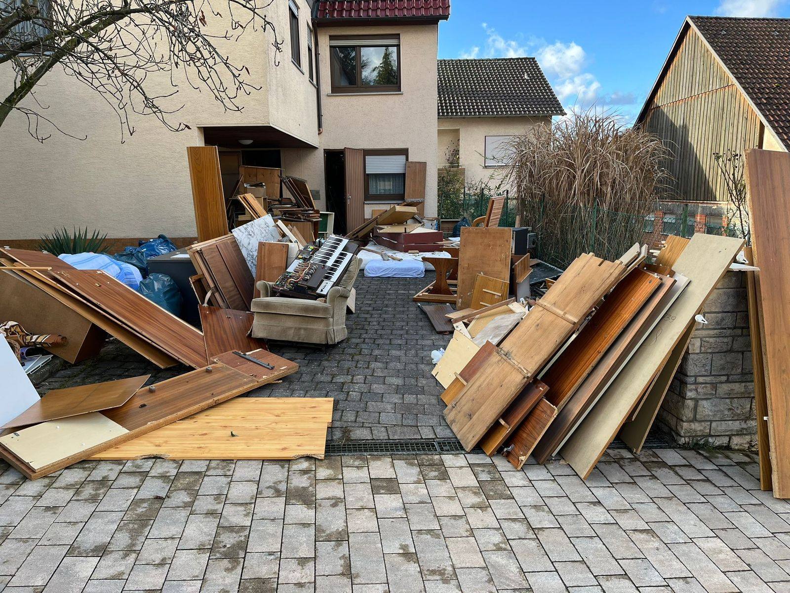 Vorher: Hofeinfahrt eines Wohnhauses in Allmersbach im Tal, voll mit abgebauten Möbeln, einer Heimorgel, einem Sessel, Matratzen und Müllsäcken